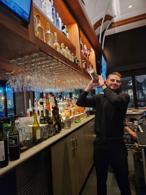 Un camarero, Daniel Vinogradov, en Del Frisco's en Fort Lauderdale, sonriendo mientras mezcla bebidas detrás de la barra.