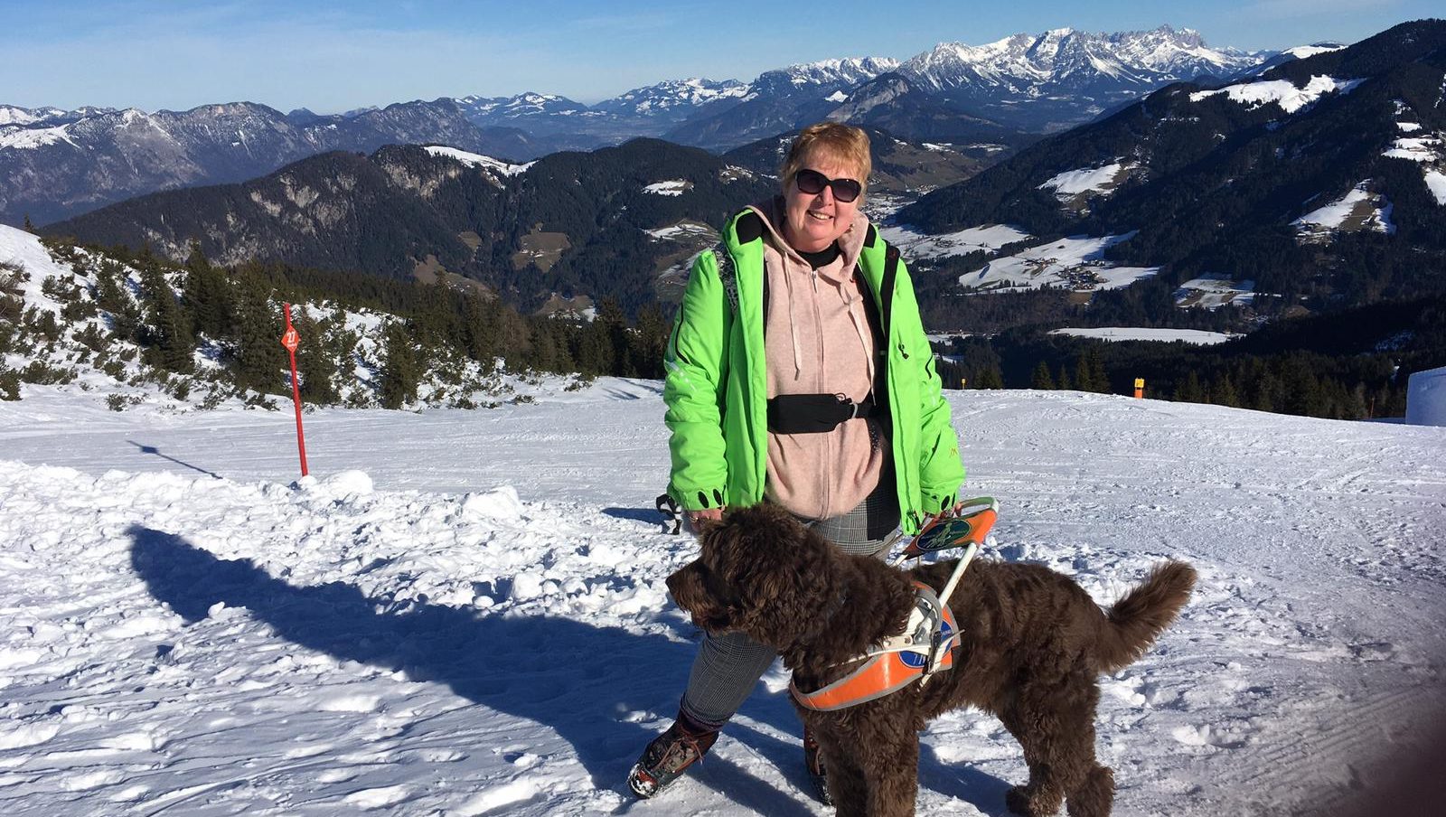Lebhafte Frau mit Blindenhund auf verschneiter Berglandschaft, genießt Outdoor-Aktivitäten.
