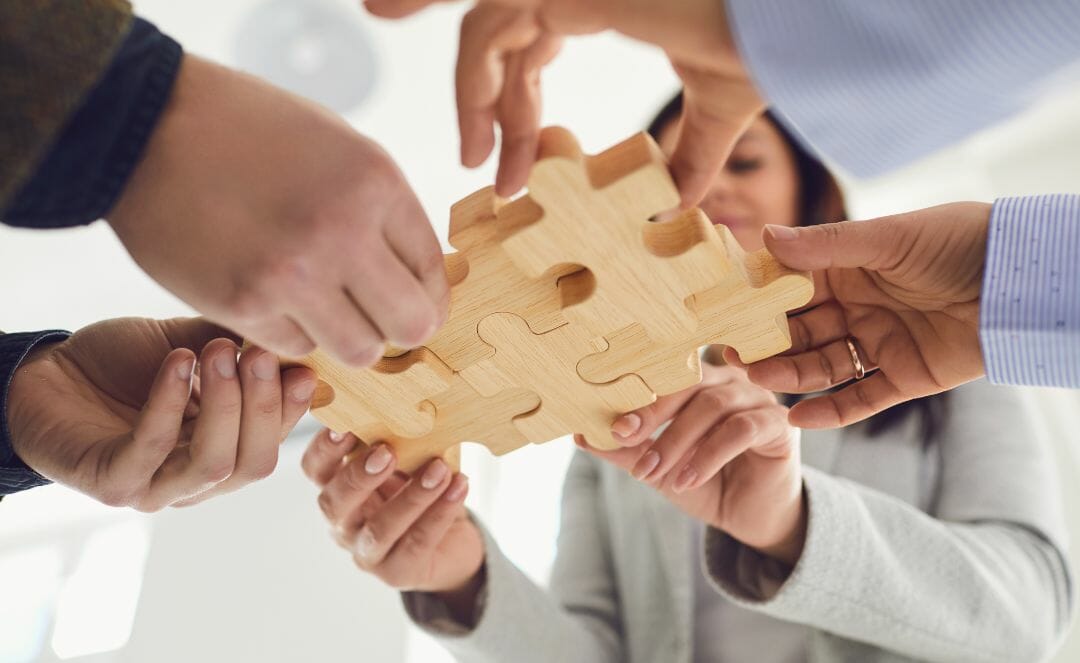 Menschen arbeiten zusammen, um große Holzpuzzleteile zusammenzusetzen, die die Zusammenarbeit in Küchengeschäften symbolisieren.
