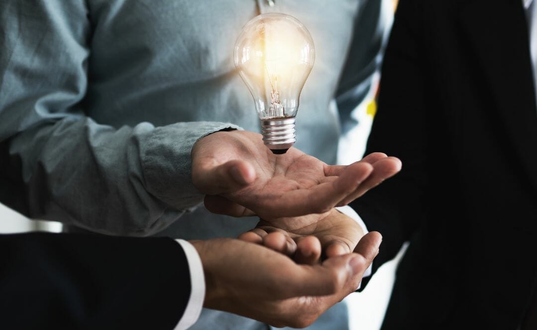 Eine Gruppe von Menschen hält eine brennende Glühbirne über ihren Händen, die die Innovation in einem modernen Badezimmergeschäft symbolisiert.