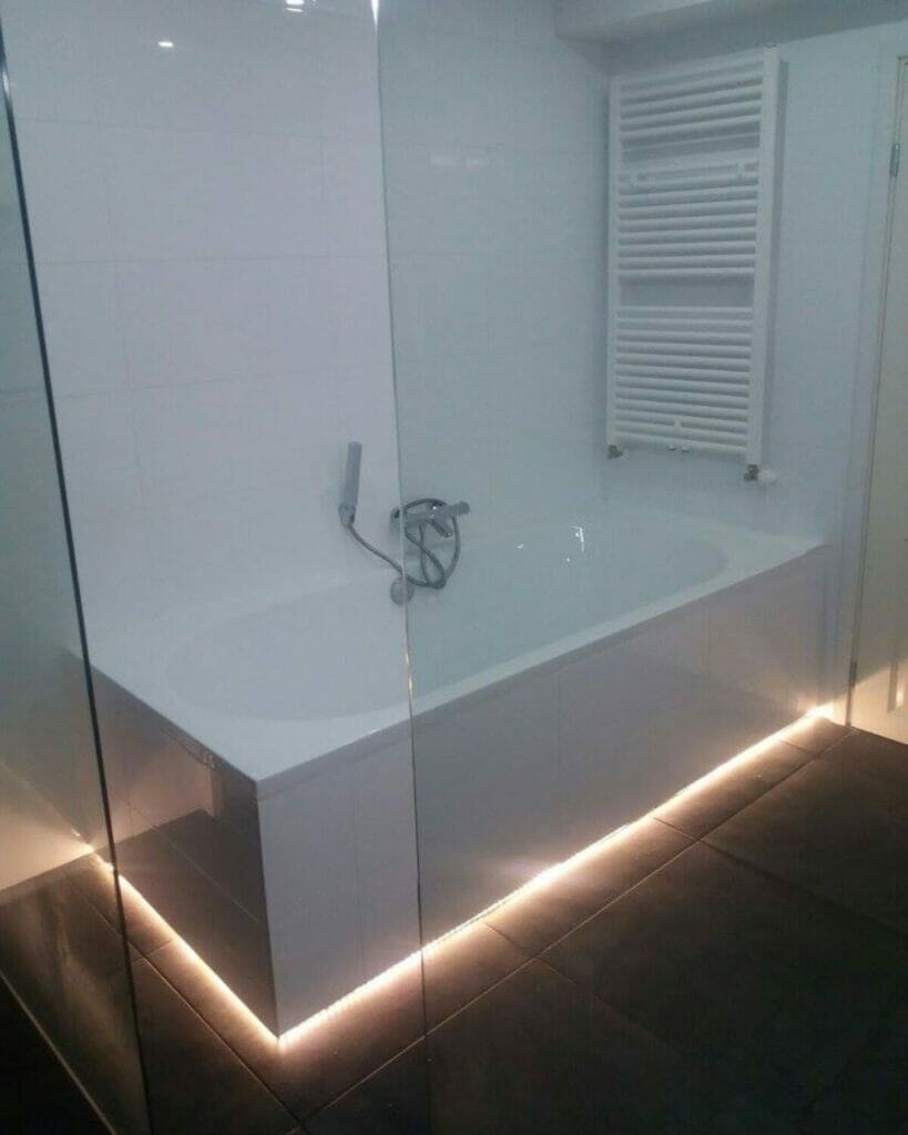 Das moderne Badezimmer verfügt über eine weiße Badewanne mit Dusche, einen beheizten Handtuchhalter und LED-Beleuchtung unter der Badewanne. Der Boden ist dunkelgrau gefliest und bietet ausgeklügelte Lösungen für die Beleuchtung des Badezimmers.