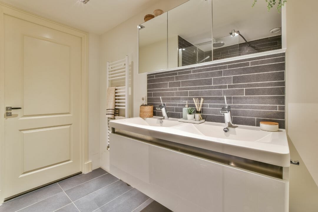 Modernes Badezimmer mit Doppelwaschbecken, Spiegelschränken, Handtuchheizkörper und grauen Fliesen. Ideal zur Inspiration in Badezimmergeschäften.