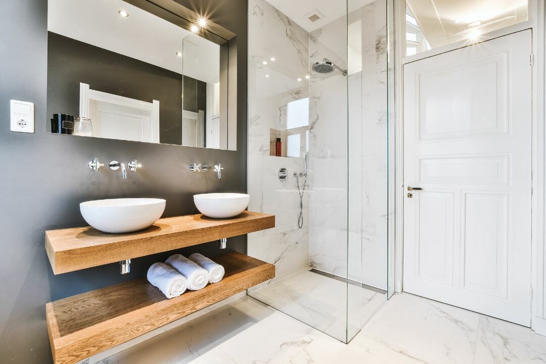 Modernes Badezimmer mit Holzwaschbecken, Marmorwänden, Duschkabine aus Glas und weißer Tür. Besuchen Sie unseren Shop für alle Ihre Renovierungsbedürfnisse.
