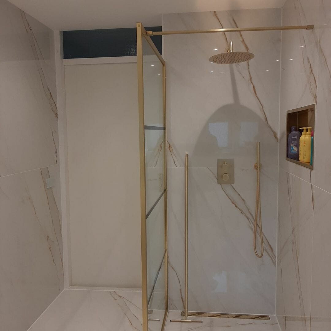 Ein geräumiges Gefühl in einem modernen Badezimmer mit einer großen Glasduschkabine mit goldenen Rahmen, umgeben von weißen Marmorwänden und -böden, die ein helles und raffiniertes Erscheinungsbild verleihen. Kundenbeispiel für modernes Duschdesign in neutralen Tönen. Baddesign, modern, Marmoroptik, Naturseusch, hell, anspruchsvoll