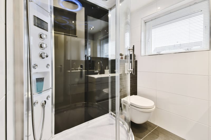 Modernes Badezimmer mit einer gläsernen Duschkabine mit mehreren Düsen, einer schwimmenden Toilette und einem Fenster mit Jalousien. Besuchen Sie Ihr örtliches Badezimmergeschäft, um sich inspirieren zu lassen oder ähnliche Setups zu finden. Digitale Duschsysteme.