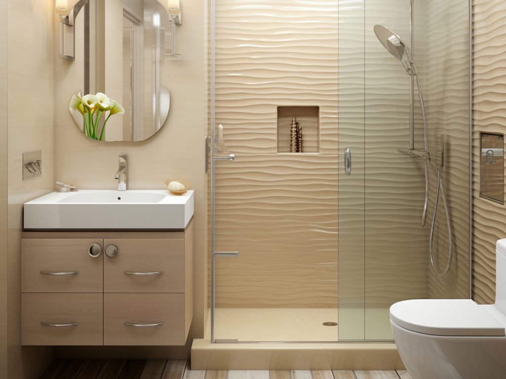 Modernes Badezimmer mit Fußbodenheizung, einer Glasdusche, beigen Strukturwänden, einem Wandwaschbecken mit Spiegel und einer Vase mit weißen Blumen auf dem Waschbecken.