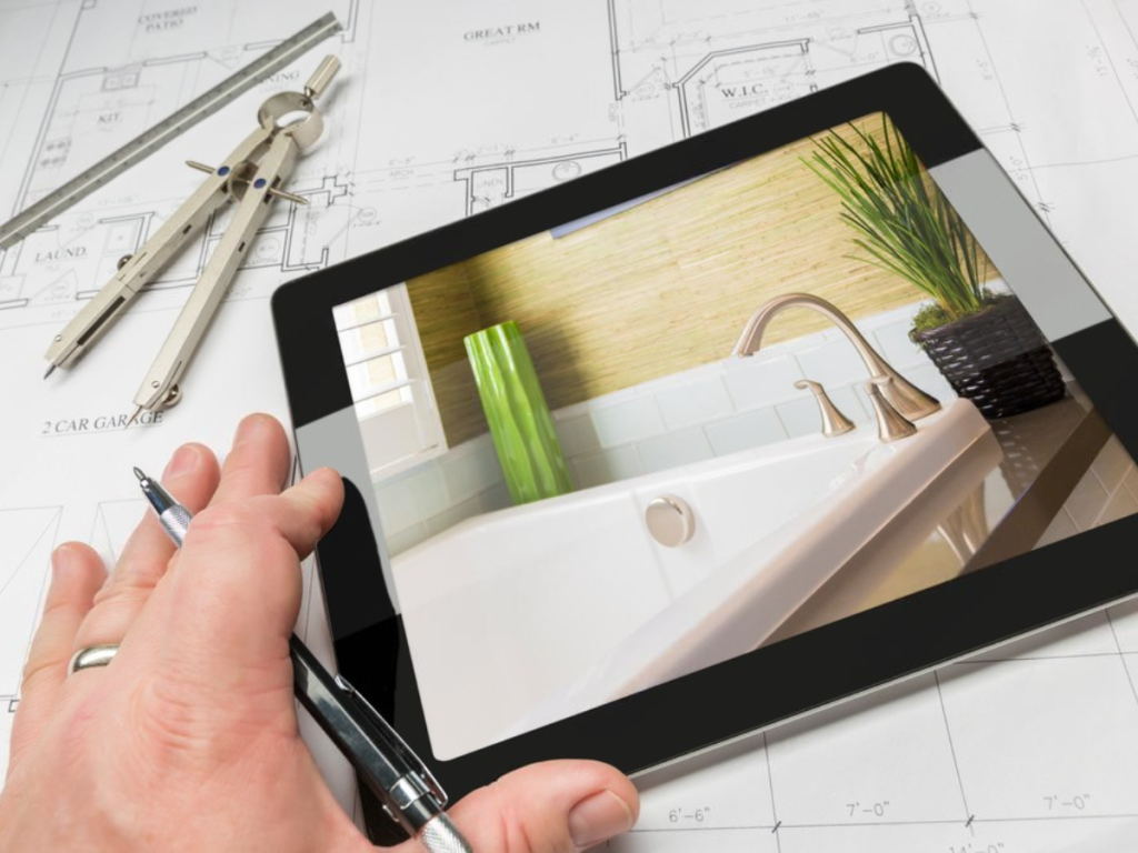 Een hand die een tablet vasthoudt, toont een badkamer met een strakke wastafel en een levendige plant, perfect geplaatst boven de architectonische blauwdrukken. Essentiële hulpmiddelen zoals een pen en kompas wijzen op een lopende badkamerrenovatie.