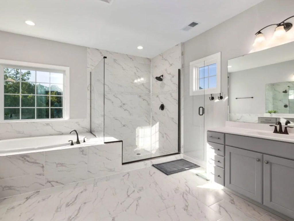 Modernes Badezimmer mit weißem Marmordesign, ausgestattet mit Badewanne, Glasdusche, großem Spiegel und grauem Waschbecken mit Tageslicht.