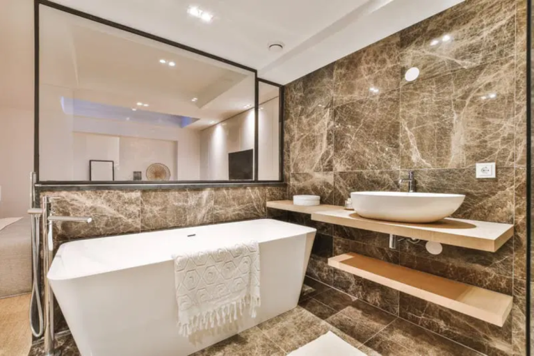 Erleben Sie ein luxuriöses Badezimmer mit modernen Marmorwänden, einer freistehenden Badewanne und einem eleganten Waschbecken.