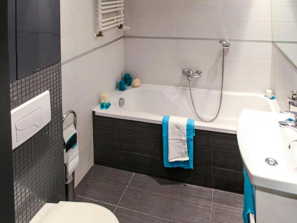 Moderne Badezimmerdesigns mit Badewanne und Dusche, Waschbecken mit Spiegel und WC, ergänzt durch Handtücher mit blauem Akzent. Ein Handtuchhalter und Toilettenartikel tragen zur Funktionalität des Raums bei und schaffen eine perfekte Mischung aus Stil und Zweckmäßigkeit.