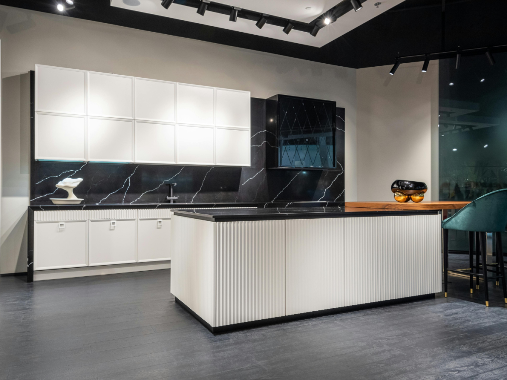 Moderne Küche mit weißen Schränken, schwarzer Marmorrückwand und einer zentralen Insel mit strukturierter Front. Dunkler Holzboden und Schienenbeleuchtung sorgen für eine elegante, elegante Atmosphäre.
