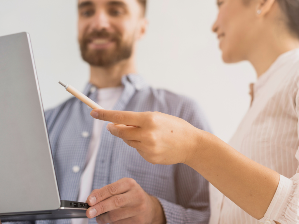 Zwei Personen schauen auf einen Laptop-Bildschirm und diskutieren über die neuesten Küchengeräte. Eine Person hält einen Stift in der Hand und zeigt auf den Bildschirm, was innovative Funktionen und schlanke Designs hervorhebt.