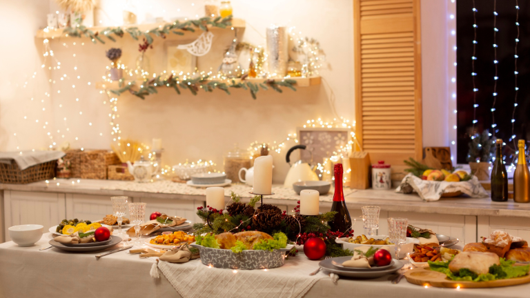 Ein festlicher Esstisch in der Traumküche ist mit Tellern mit Speisen, Kerzen und Weihnachtsdekoration gedeckt. Regale im Hintergrund sind mit Lichterketten und saisonaler Dekoration verziert.