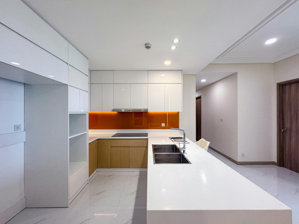 Moderne Küche mit weißen Schränken, einer orangefarbenen Rückwand und einer Insel mit Spüle. Marmorböden ergänzen den Raum, während eine Holztür im Hintergrund für Wärme sorgt. Ideal für Küchen- und Badliebhaber, die Stil und Funktionalität schätzen.