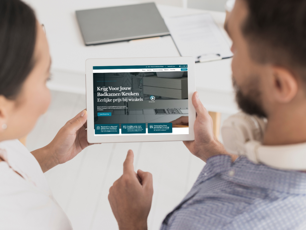Zwei Personen schauen auf ein Tablet mit einer Website auf Niederländisch mit Informationen über Küchen, Bäder und die neuesten Trends bei Küchengeräten.
