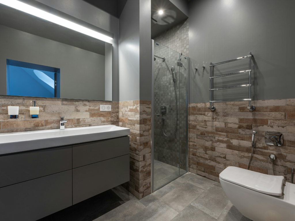 Greifen Sie die Trends im Badezimmer mit einem modernen Badezimmer mit grauen und unverputzten Ziegelwänden auf. Dieses Badezimmer verfügt über einen großen Spiegel, eine schlanke Arbeitsplatte mit Waschbecken, eine Duschkabine aus Glas und eine stilvolle Wandtoilette, die zeitgenössische Designelemente harmoniert.