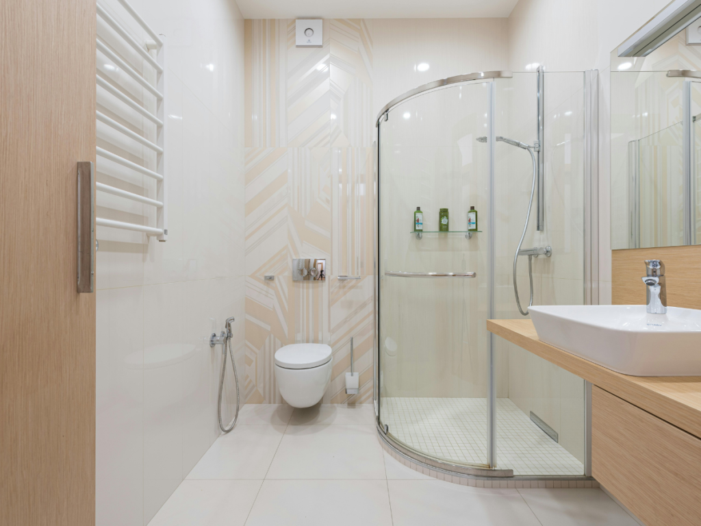Modernes Badezimmer mit Glasdusche, Wandschrank und weißem Waschbecken auf einer Holzarbeitsplatte. Beigefarbene Fliesenakzente ergänzen das schlanke Design, während ein effizientes Rohrleitungsdiagramm für eine nahtlose Funktionalität sorgt.