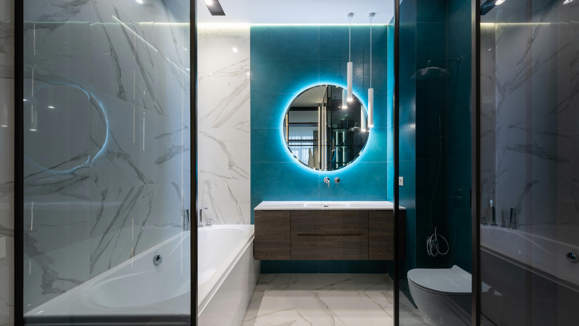 Ein elegantes, modernes Badezimmer mit Badewanne, dunklen Fliesen und einem runden Spiegel mit blauer LED-Beleuchtung über einem Holzwaschbecken erweckt Ihre Vision für eine Badezimmerrenovierung zum Leben.