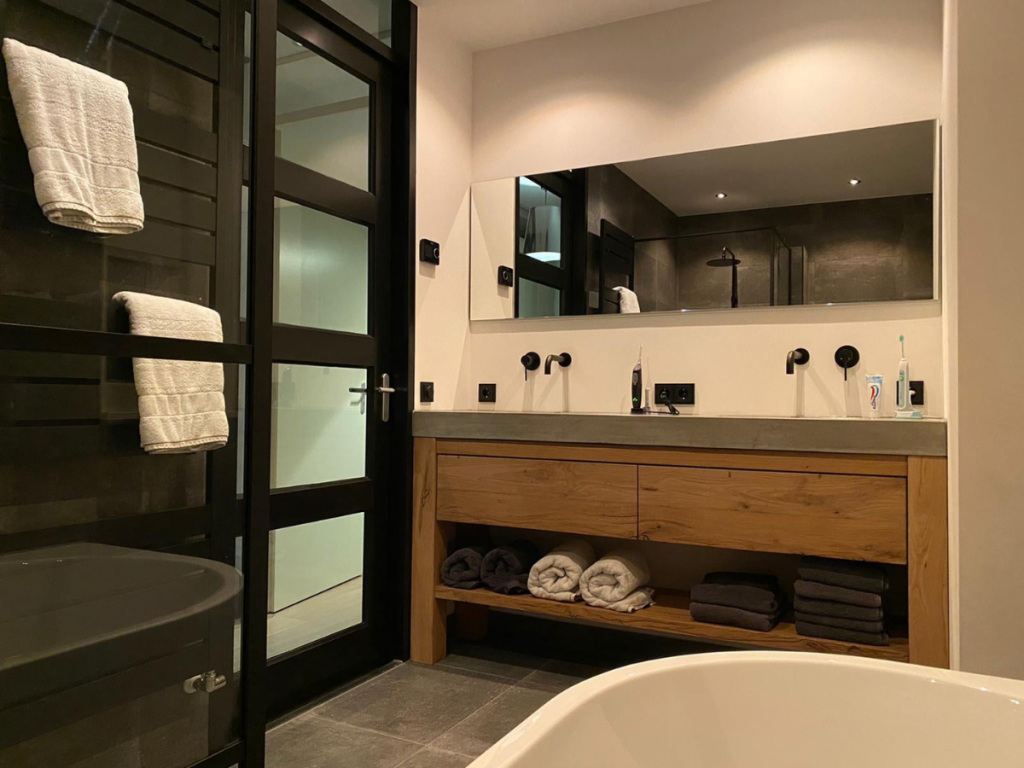 Modernes Badezimmer im Jahr 2025 mit Doppelwaschbecken, großem Spiegel und Holzschrank. Die Handtücher sind ordentlich angeordnet und im Hintergrund ist eine begehbare Dusche zu sehen, die Stil und Funktionalität nahtlos miteinander verbindet.