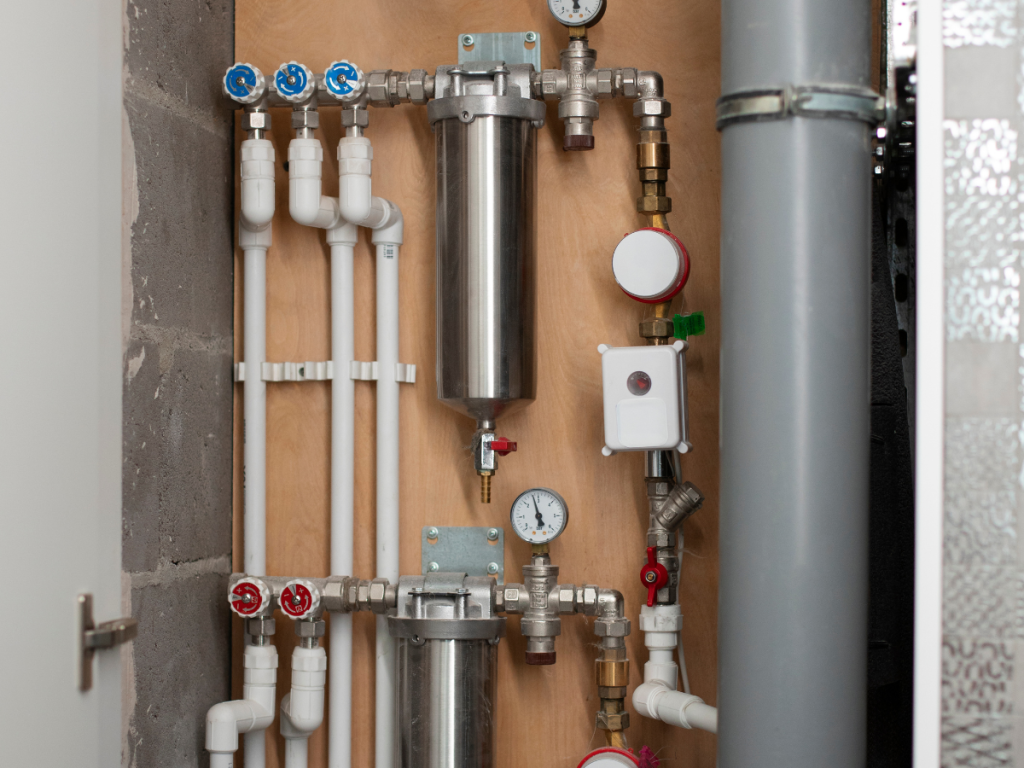 Ein Sanitärsystem mit verschiedenen Rohren, Manometern und Ventilen ist ordentlich auf einem Holzbrett angeordnet.