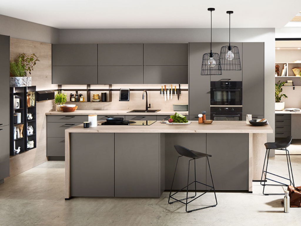 Moderne Küche mit grauen Schränken, einer zentralen Insel, Barhockern und hängenden Drahtrahmenlampen. Einbaugeräte spiegeln die neuesten Trends bei Küchengeräten wider, während auf der Arbeitsplatte frisches Gemüse und elegante Utensilien präsentiert werden.