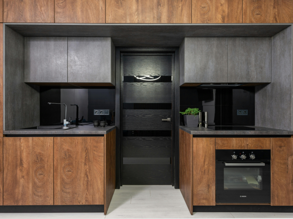 Moderne Küche mit dunklen Holzschränken, schwarzen Arbeitsplatten, einem Backofen, einer Spüle und einer Topfpflanze. Die Tür in der Mitte hat ein schlankes, minimalistisches Design, das an eine elegante Installationszeichnung erinnert.