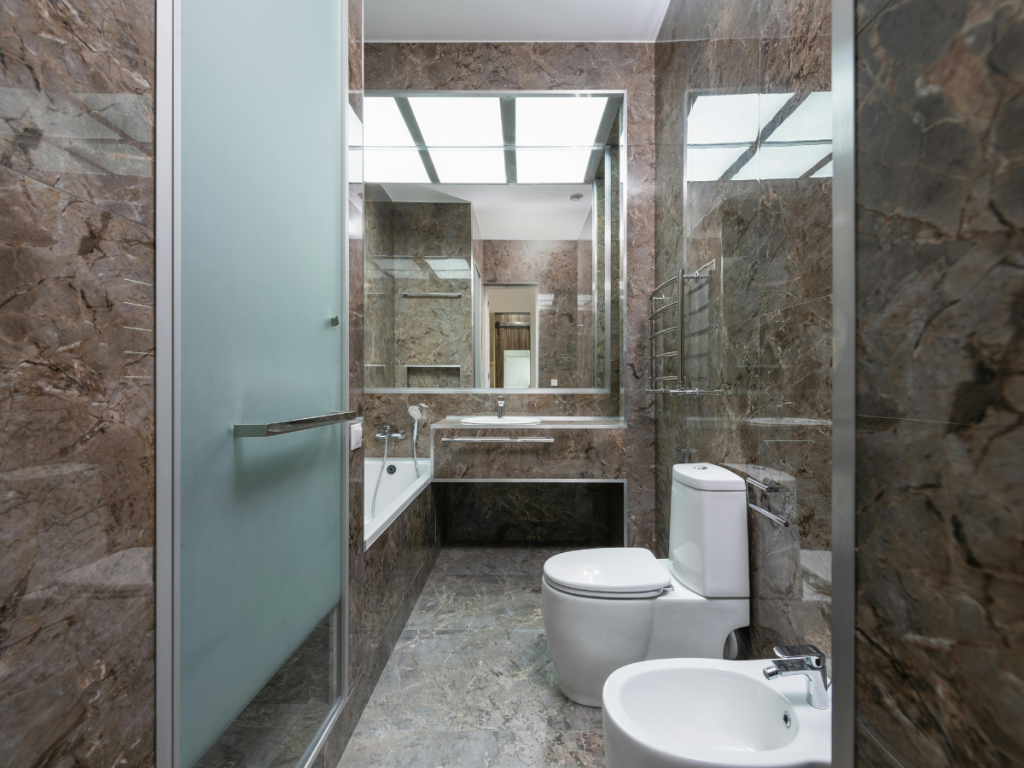 Dit eigentijdse badkamerontwerp heeft strakke bruine marmeren muren en vloeren, aangevuld met een stijlvol toilet, bidet en een bad met een glazen wand. Een grote spiegel en handdoekrek dragen bij aan de moderne uitstraling van de badkamer.