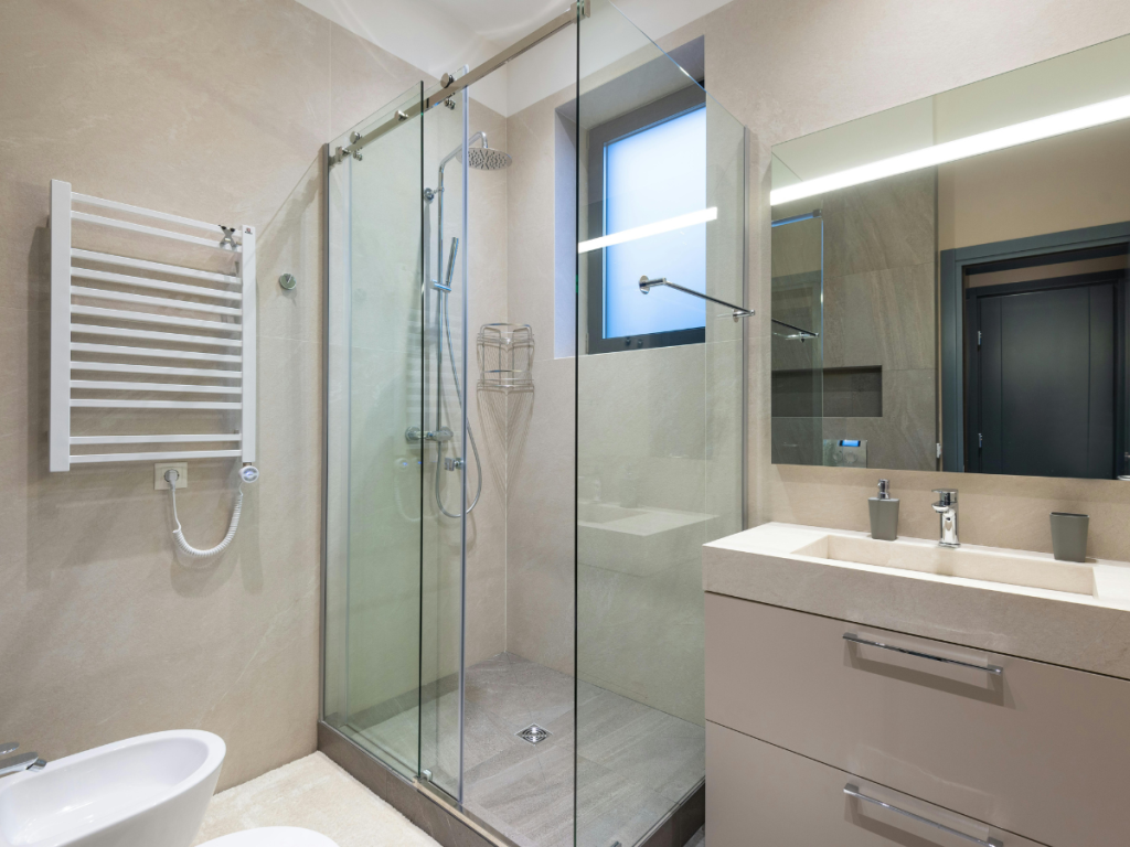Modernes Badezimmer mit einer Duschkabine aus Glas, einem großen Spiegel, einem Waschbecken mit Schubladen, einem Handtuchheizkörper an der Wand und einem Fenster für Tageslicht und Belüftung.