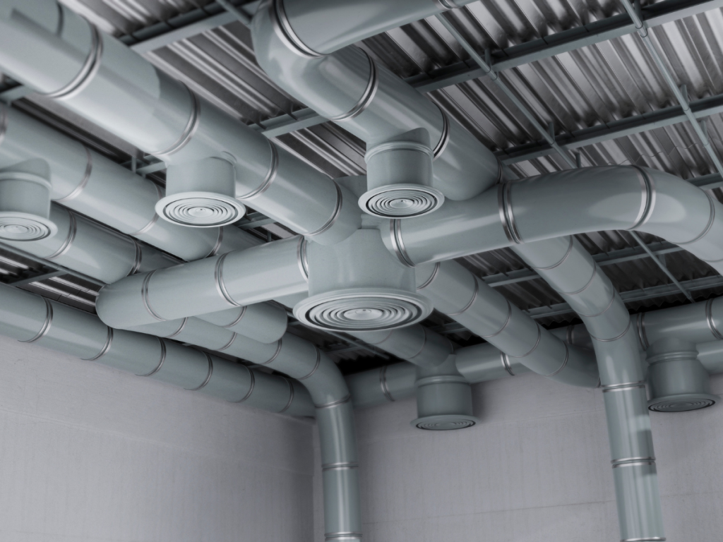 Ein Netzwerk aus grauen Metallluftkanälen, die in einer Decke installiert sind, verfügt über kreisförmige Lüftungsschlitze, die nahtlos in eine gerippte Metalldeckenstruktur integriert sind, um eine effiziente Belüftung zu gewährleisten.