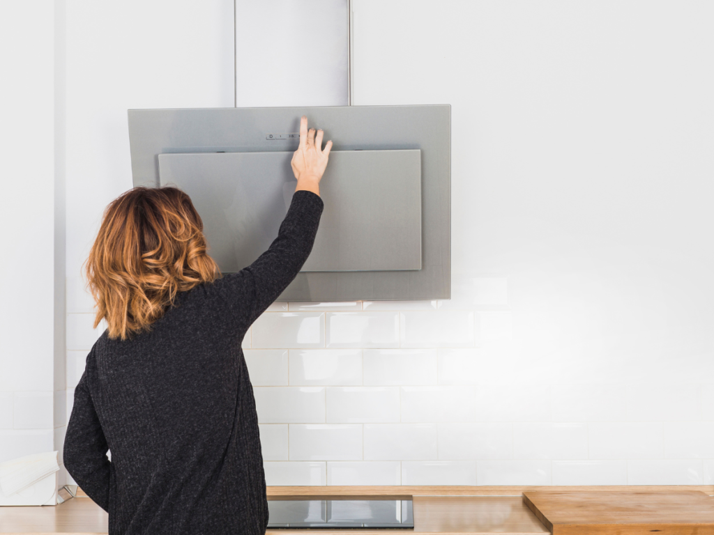 Eine Person mit schulterlangen braunen Haaren schaltet auf Knopfdruck eine an der Wand montierte Dunstabzugshaube ein und hält so die Küche während des Kochens frisch und belüftet.