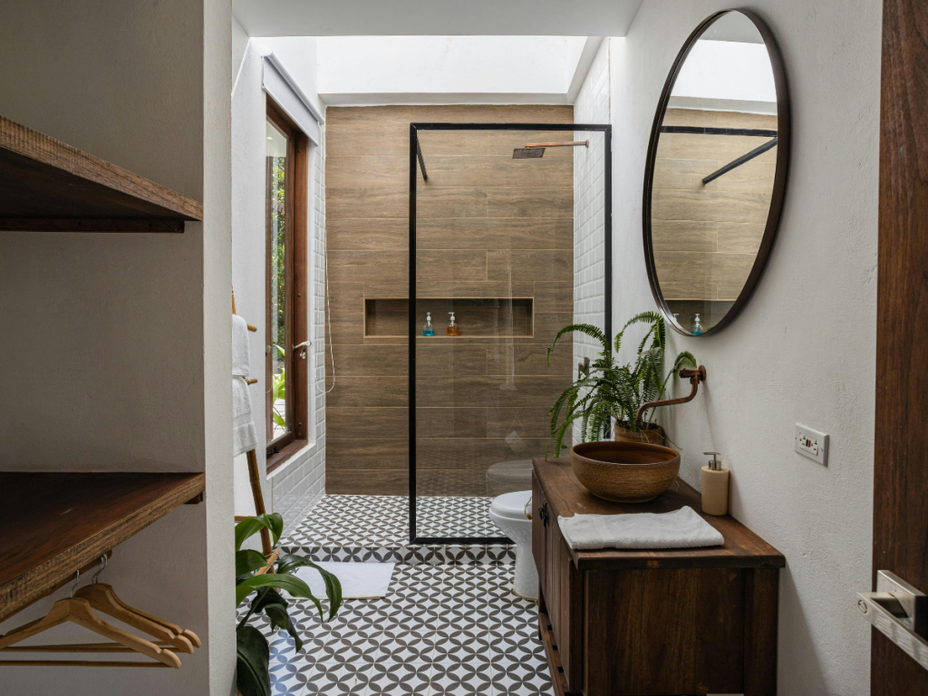 Modernes Badezimmer im eklektischen Stil mit gemustertem Fliesenboden, Duschkabine aus Glas, rundem Spiegel, Holzwaschtisch mit Waschbecken, Zimmerpflanzen und natürlichem Licht durch das große Fenster.