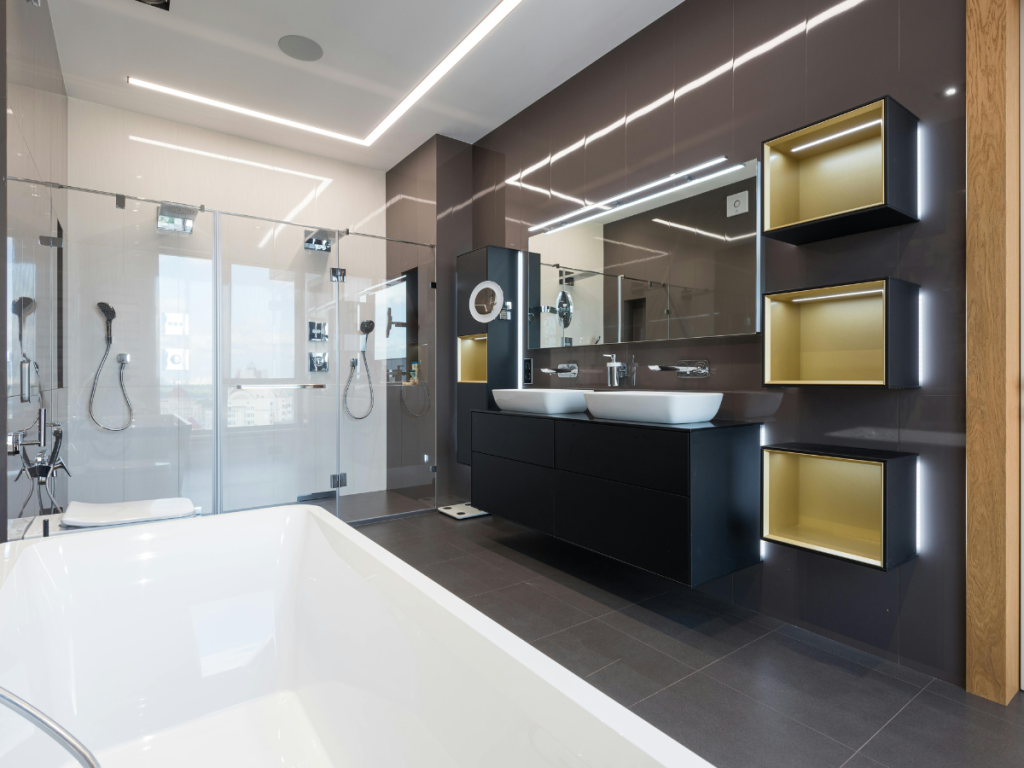 Modernes Badezimmer mit großer Badewanne, Doppelwaschbecken, Glasdusche, Wandregalen und einem großen Spiegel mit heller Beleuchtung.