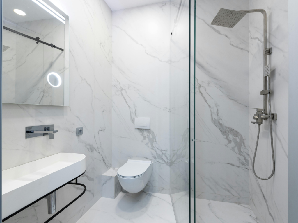 Modernes Badezimmer mit weißen Marmorwänden, einem wandhängenden Waschbecken, einer schwimmenden Toilette, eleganter Beleuchtung, einer Glasdusche und einem quadratischen Regenduschkopf.