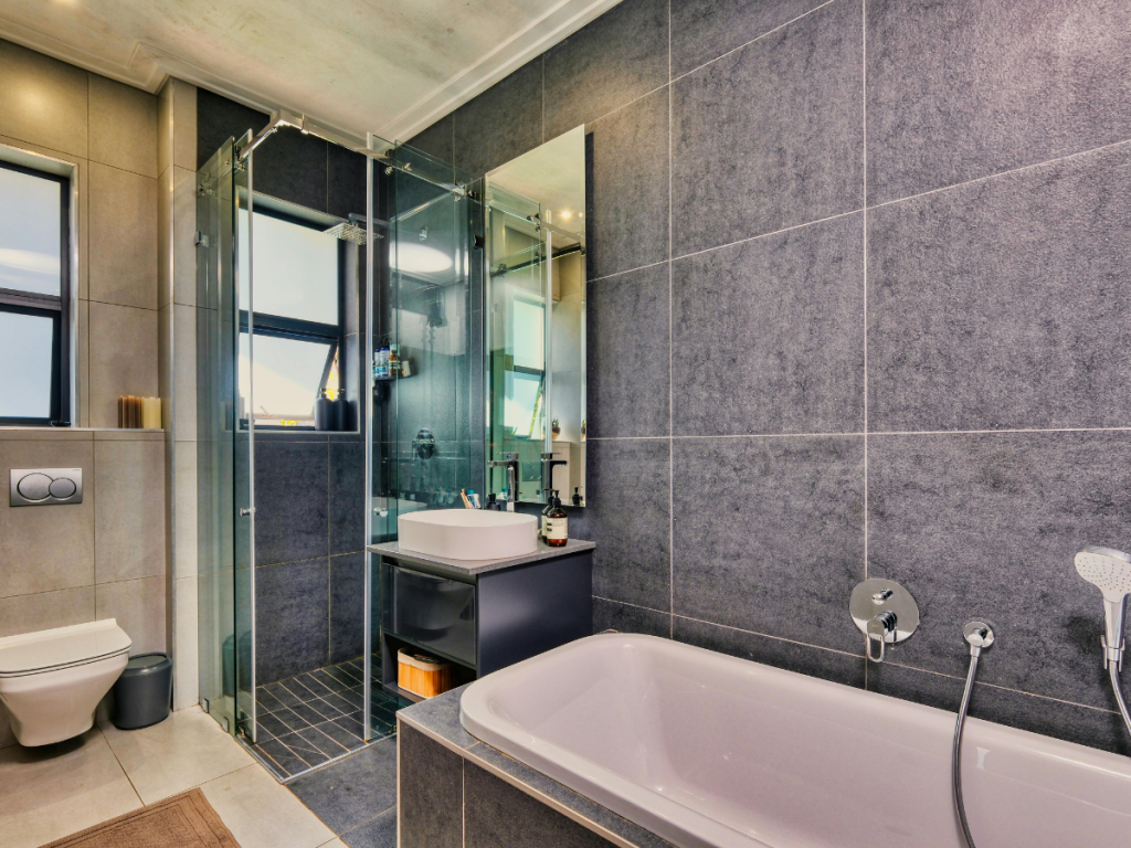 Modernes Badezimmer mit einer Glasdusche, einer Badewanne, einer hängenden Toilette, einem großen Spiegel und grau gefliesten Wänden. Entworfen mit Blick auf Komfort und Stil, zugeschnitten auf das Feedback der Kunden.