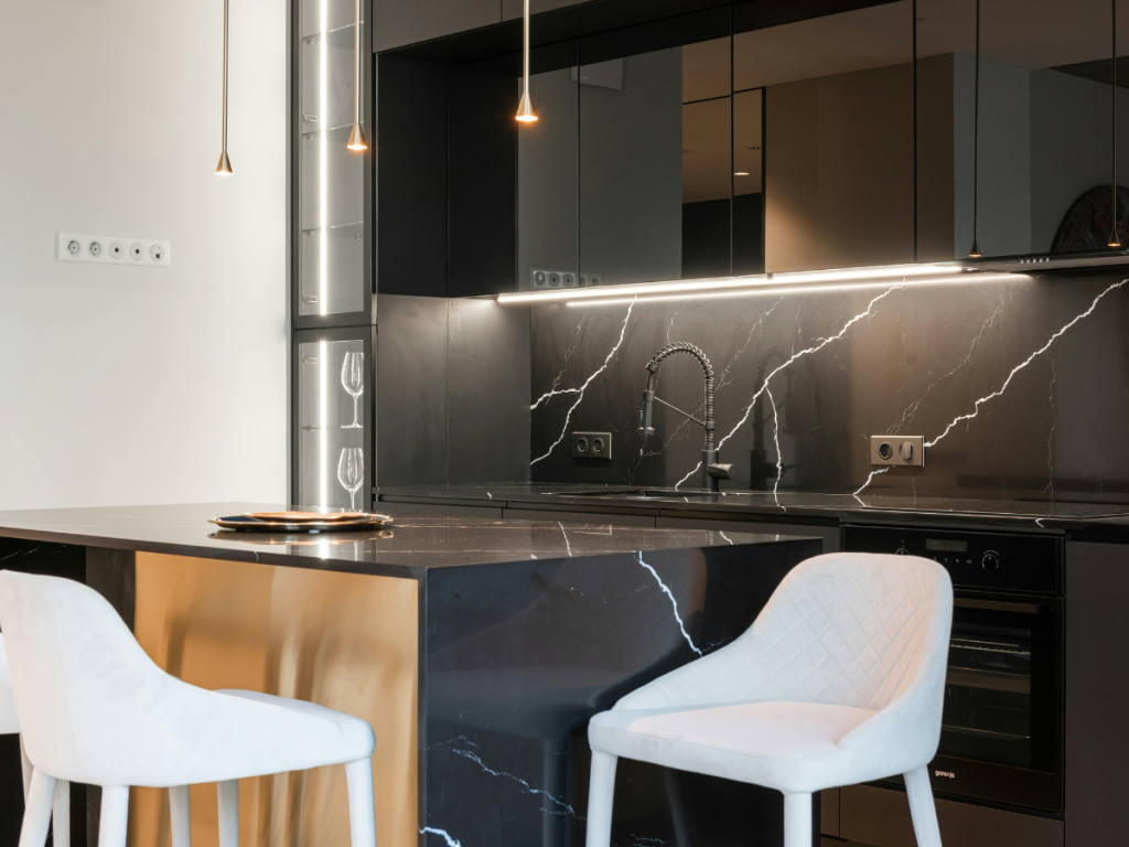 Moderne Küche mit Arbeitsplatte und Rückwand aus schwarzem Marmor, weißen gepolsterten Stühlen, eingebautem Backofen, Unterschrankbeleuchtung und offenen Regalen für stilvolle Aufbewahrung.