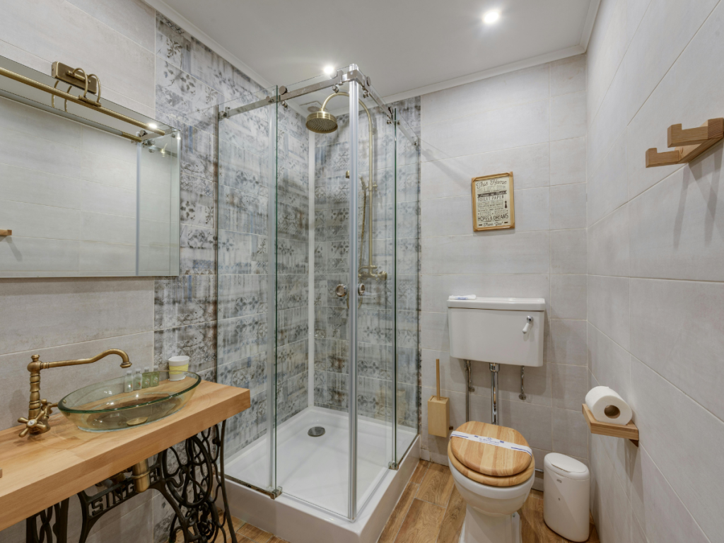 Modernes Badezimmer im eklektischen Stil mit einer Duschkabine aus Glas, einer hängenden Toilette mit Holzsitz, einem Waschbecken auf einer Holzplatte und neutral gefliesten Wänden und Böden.