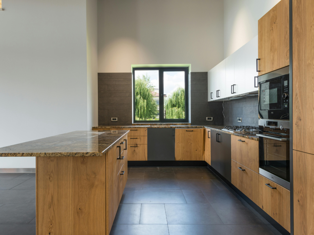 Moderne Küche mit Holzschränken, Granit-Arbeitsplatten, eingebautem Backofen, Herd, Geschirrspüler und einem Fenster mit Blick ins Grüne: perfekt für Liebhaber moderner Küchen.