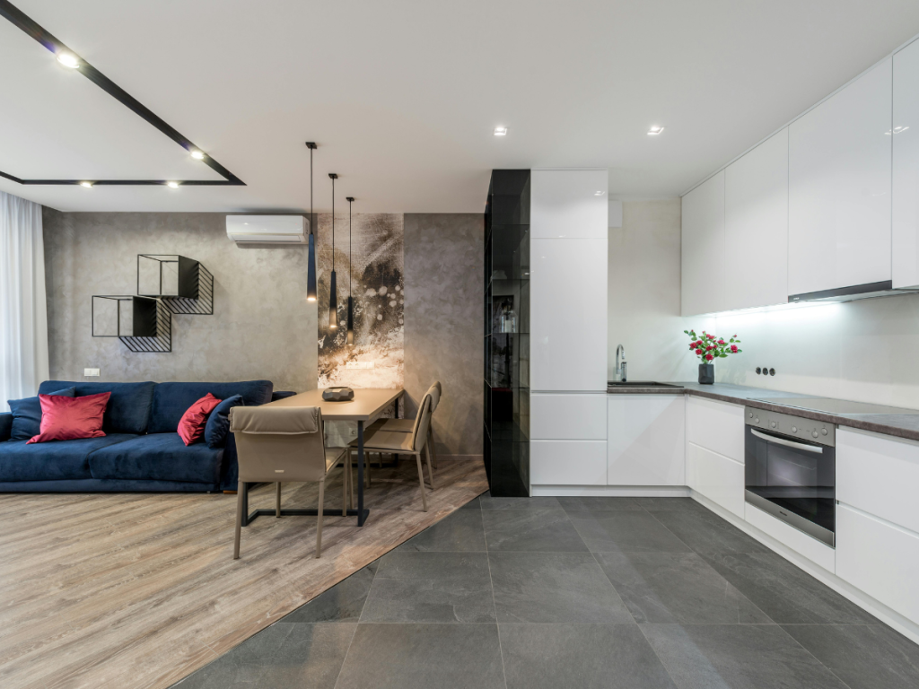 Moderne, open leefruimte met een marineblauwe bank, eettafel, wandkunst en een witte keuken met stijlvolle vloerpatronen, inbouwapparatuur en onderkastverlichting.