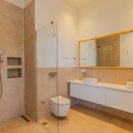 Modernes Badezimmer mit ebenerdiger Dusche, schwimmender Toilette, Doppelwaschbecken mit großem Spiegel und beige gefliesten Wänden und Fußboden, wo ruhige Farbpaletten eine beruhigende Atmosphäre schaffen.