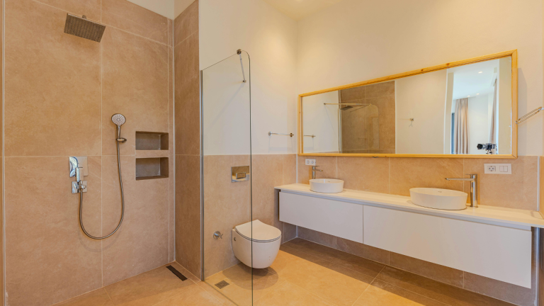 Modernes Badezimmer mit ebenerdiger Dusche, schwimmender Toilette, Doppelwaschbecken mit großem Spiegel und beige gefliesten Wänden und Fußboden, wo ruhige Farbpaletten eine beruhigende Atmosphäre schaffen.