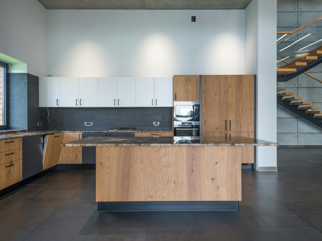 Moderne Küche mit Holzschränken, Granit-Arbeitsplatten, Edelstahlgeräten und einer Kücheninsel – perfekt für eine gemütliche Küche beim Kochen. Rechts ist eine Treppe mit Holzstufen zu sehen.