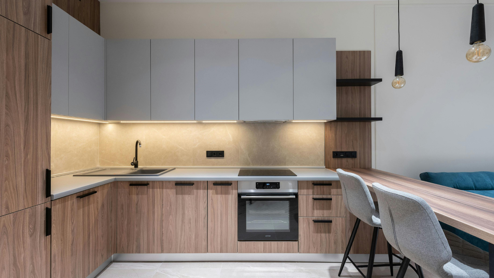 Moderne Küche mit Holz- und grauen Schränken, Einbaubackofen, Elektroherd, Unterschrankbeleuchtung, Bar mit zwei grauen Stühlen und Pendelleuchten - perfekte Inspiration für DIY-Projekte.