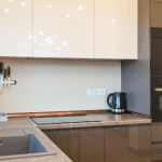 Moderne Küche für kleine Küchen, mit beigen Schränken, grauer Arbeitsplatte, eingebautem Bosch-Backofen und Kaffeemaschine, Elektroherd, Wandflügeln und einer schlanken Spüle mit Wasserhahn.