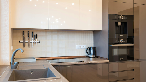 Moderne Küche für kleine Küchen, mit beigen Schränken, grauer Arbeitsplatte, eingebautem Bosch-Backofen und Kaffeemaschine, Elektroherd, Wandflügeln und einer schlanken Spüle mit Wasserhahn.