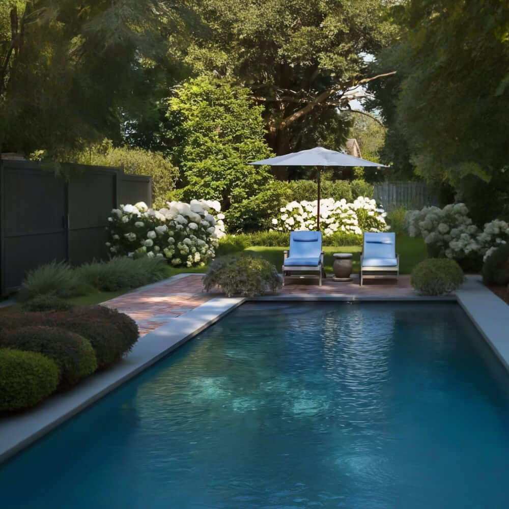 A nossa empresa projeta áreas exteriores em torno de piscinas, incorporando elementos como um pátio de pedra com duas espreguiçadeiras e um guarda-sol. A área é cercada por vegetação exuberante e flores brancas, dando ao jardim uma estética clássica e calmante. Pretendemos criar um ambiente harmonioso que convide ao relaxamento, respeitando a história e o carácter intemporal do lugar.
