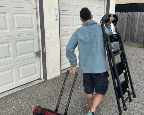 carlos garage door technician carrying a stair to service a garage door in huntington beach