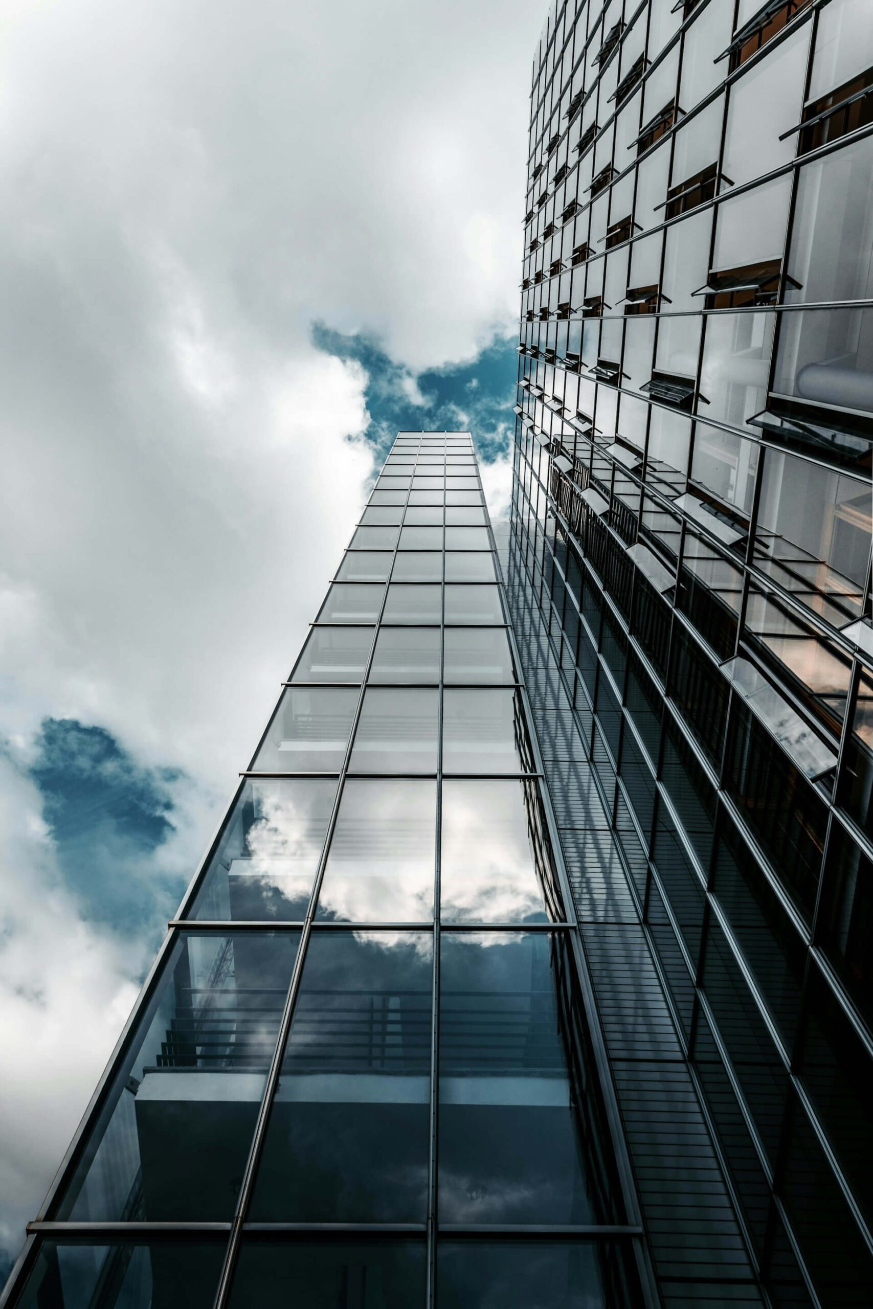 Import resale Cross-border EC Low angle view of a modern glass-walled skyscraper reflecting clouds and blue sky.