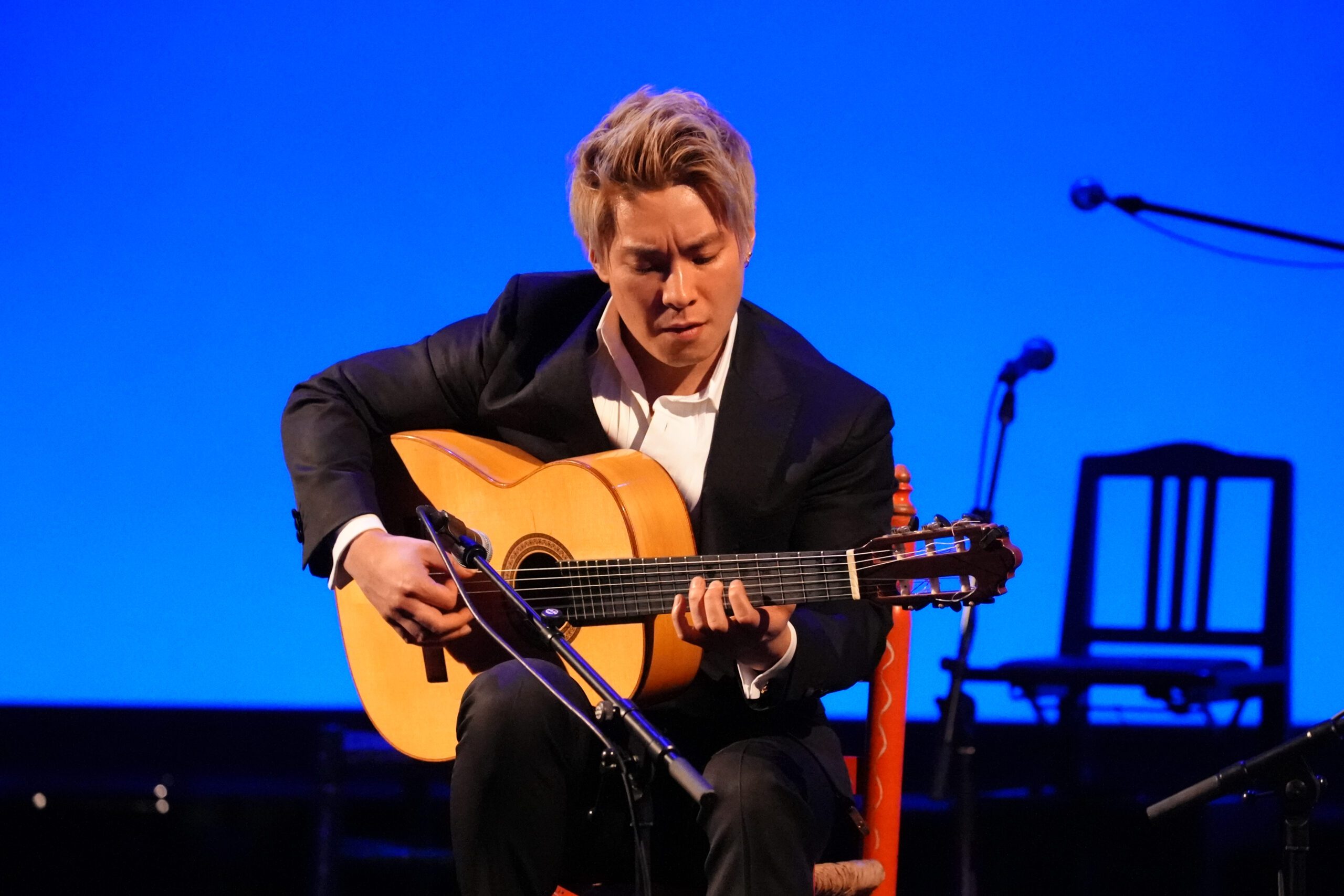 A man in a suit playing an acoustic guitar.