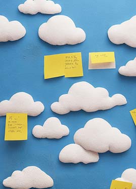 A creative pinboard with cloud-shaped cutouts and yellow sticky notes against a blue background.