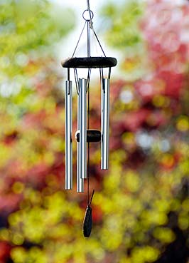 A winding path through a lush green forest with a high wind chime on one side.